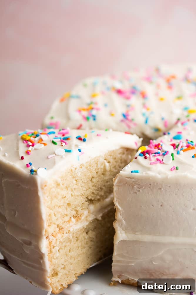 Close up of a slice of vanilla cake being removed from the cake, showcasing its moist texture and perfect crumb.
