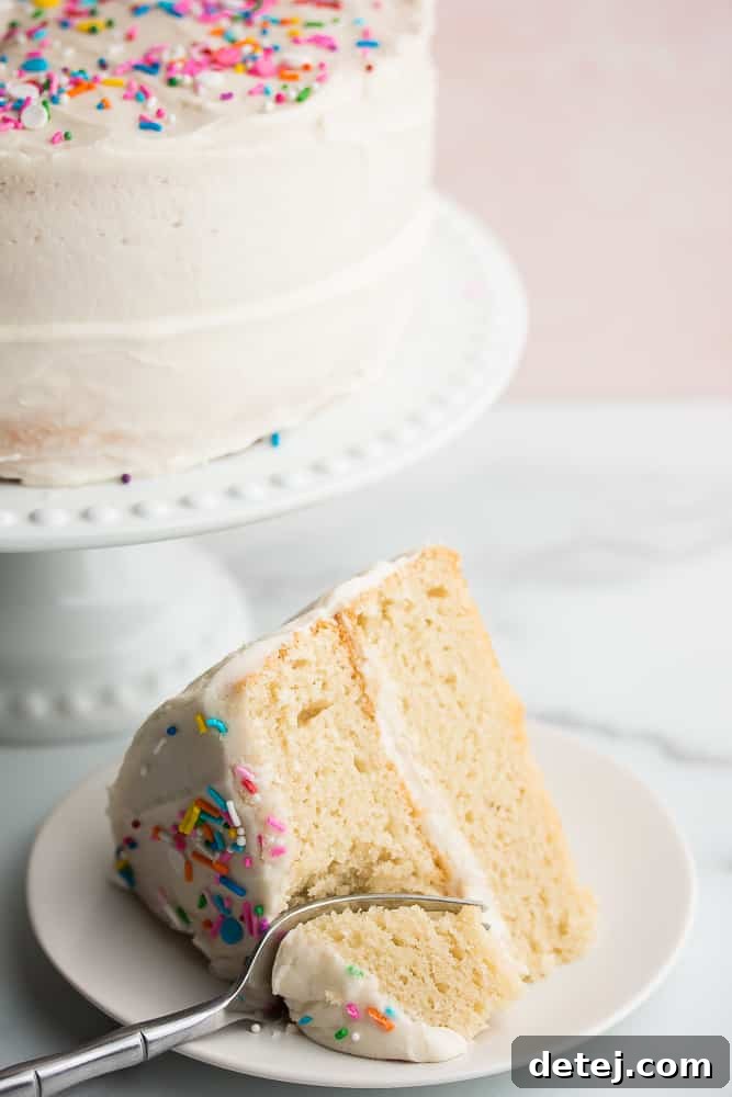 A fork taking a bite out of a generous slice of white cake on a simple white plate, highlighting the cake's soft and moist texture.