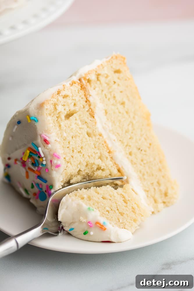 Close up of a slice of white cake with a fork taking a bite, emphasizing the soft and airy texture.
