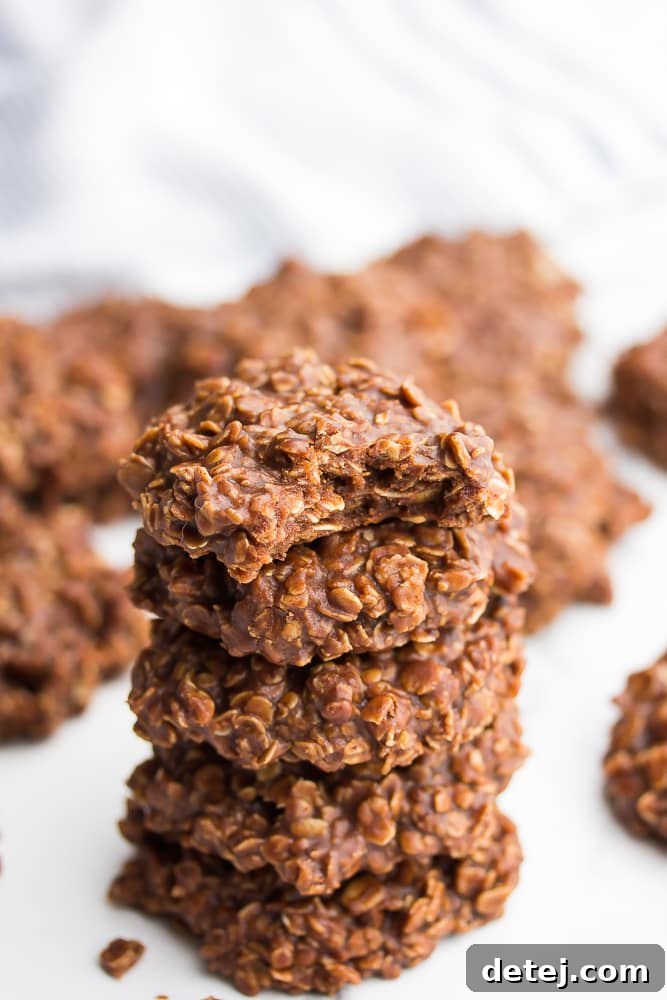 Close up of 5 vegan no bake cookies stacked on top of each other with a bite out of 1 cookie, showing its rich, soft interior.