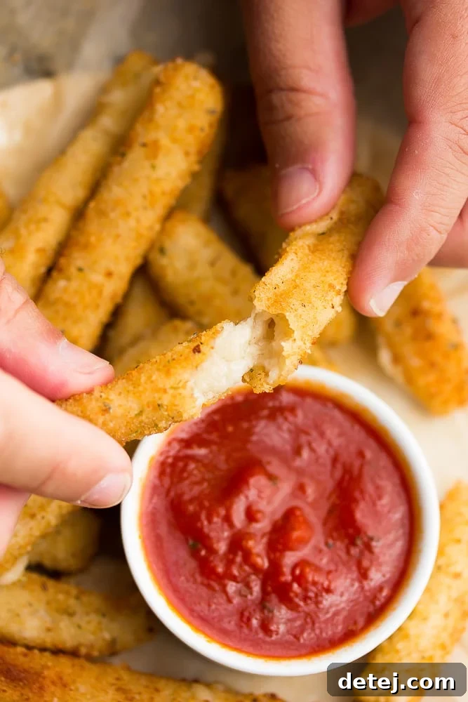 hands holding a fried cheese stick pulling it apart showing the melted vegan cheese stretch