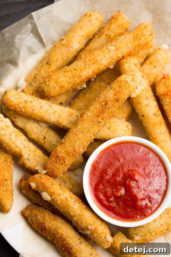 a platter of golden-fried vegan mozzarella sticks with a bowl of marinara dipping sauce