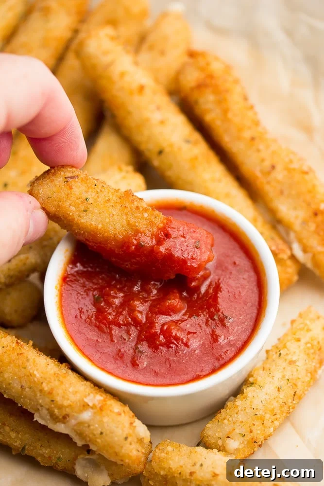 a vegan mozzarella stick being dipped into marinara sauce