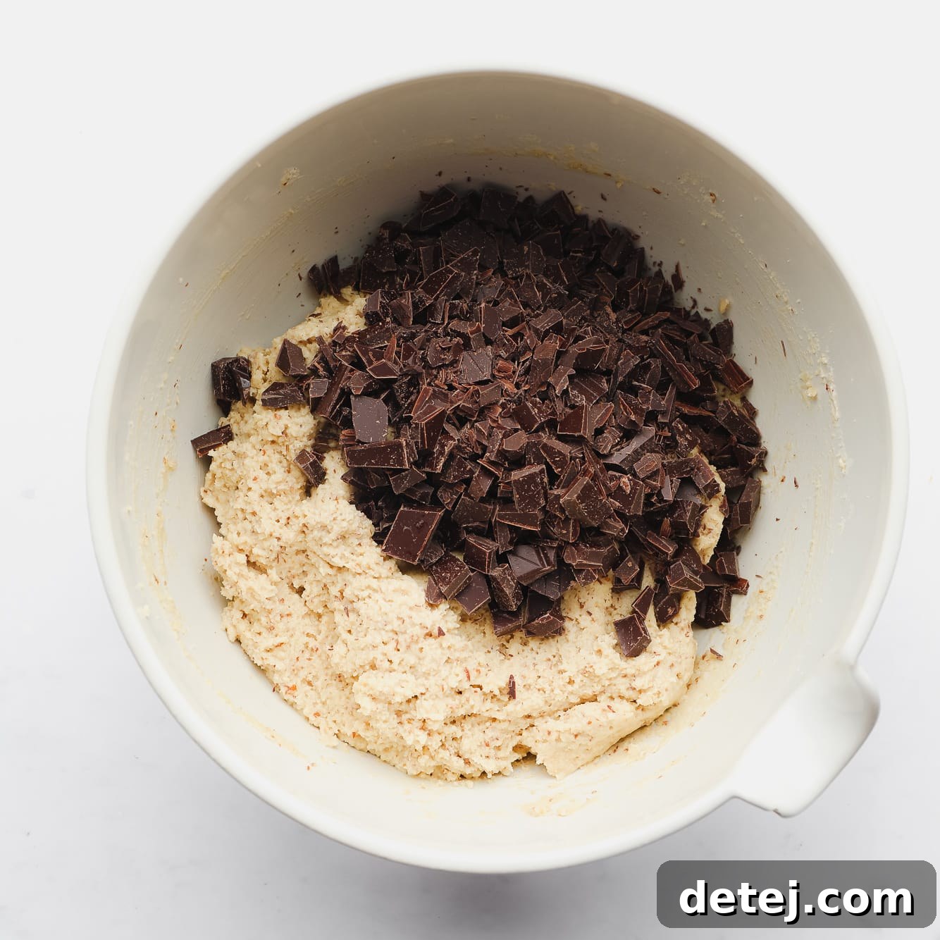 chopped chocolate on top of almond flour cookie dough in a large white bowl.