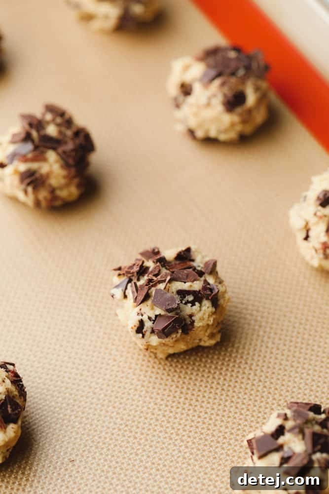close up on raw chocolate chip cookie dough balls on a parchment-lined baking sheet.