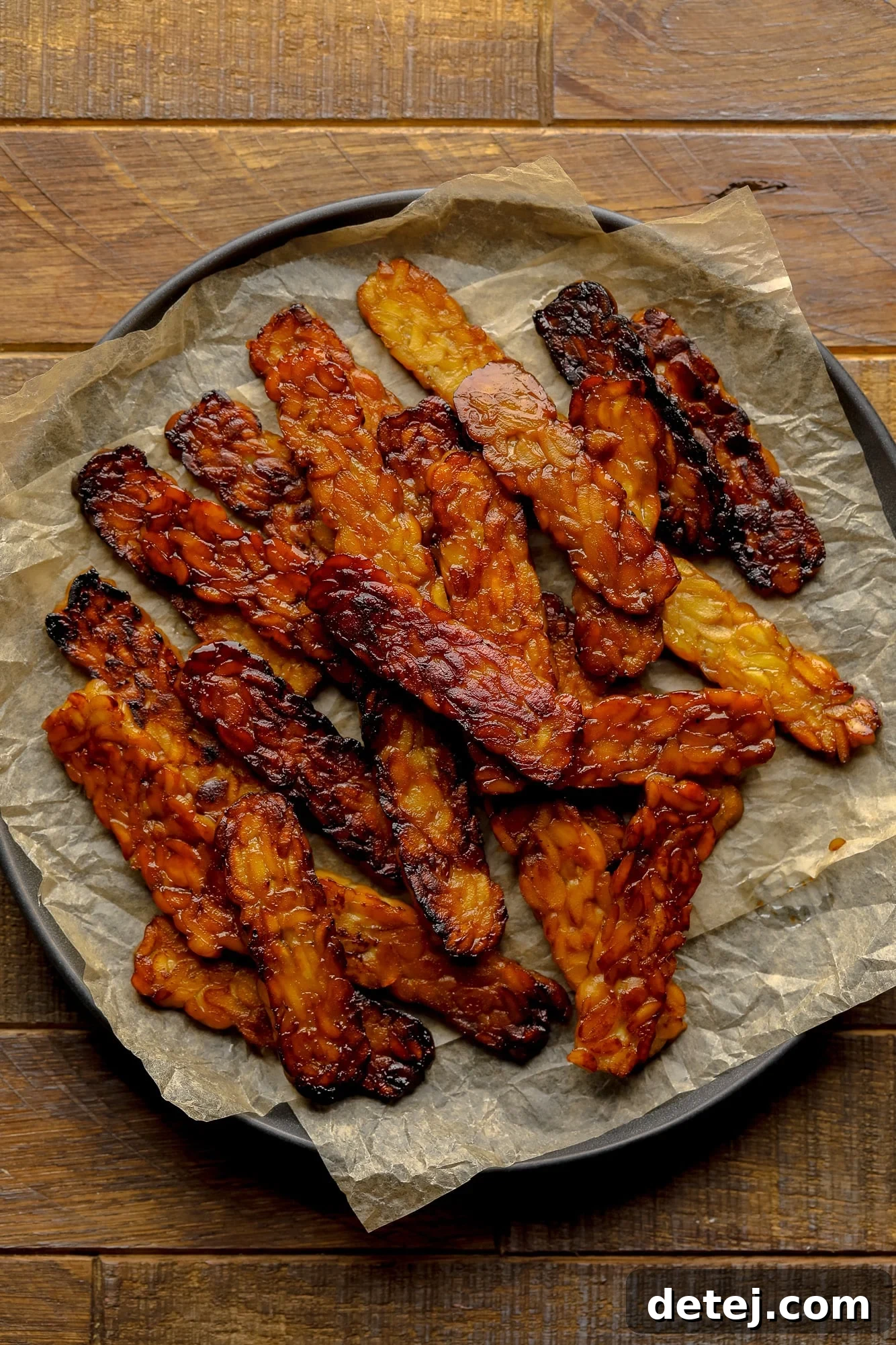 A perfectly pan-fried pile of golden-brown vegan Tempeh Bacon slices, ready to be enjoyed in sandwiches or as part of a hearty breakfast.