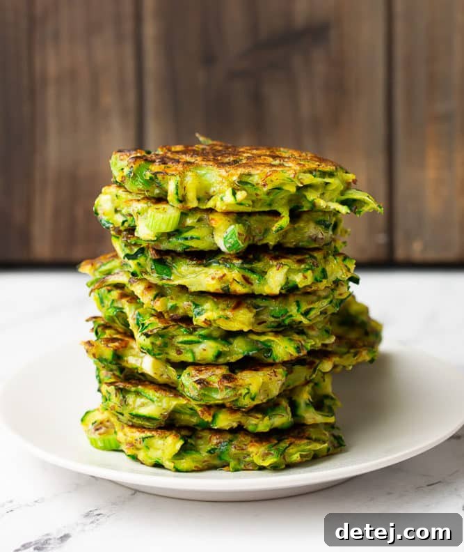 A stack of golden-brown vegan zucchini fritters neatly arranged on a pristine white plate, garnished with fresh herbs.
