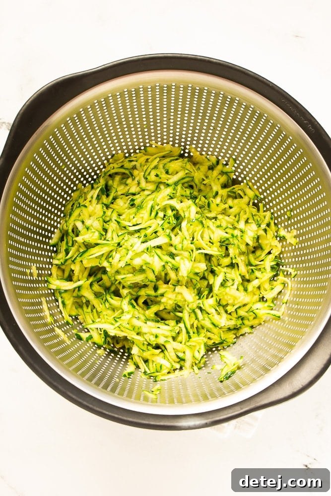 Freshly grated zucchini sitting in a strainer over a bowl, illustrating the essential moisture-draining process.