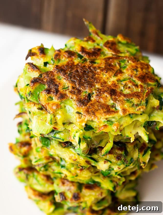 A close-up view of perfectly cooked and stacked vegan zucchini fritters, showing off their textured, golden-brown crust.