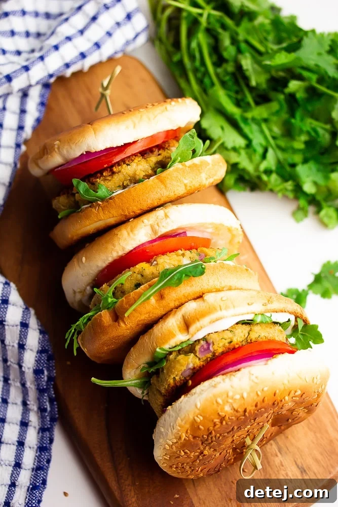 Three golden-brown chickpea burgers elegantly arranged on their sides on a cutting board, garnished with fresh tomatoes and peppery arugula, ready to be assembled into delicious sandwiches.