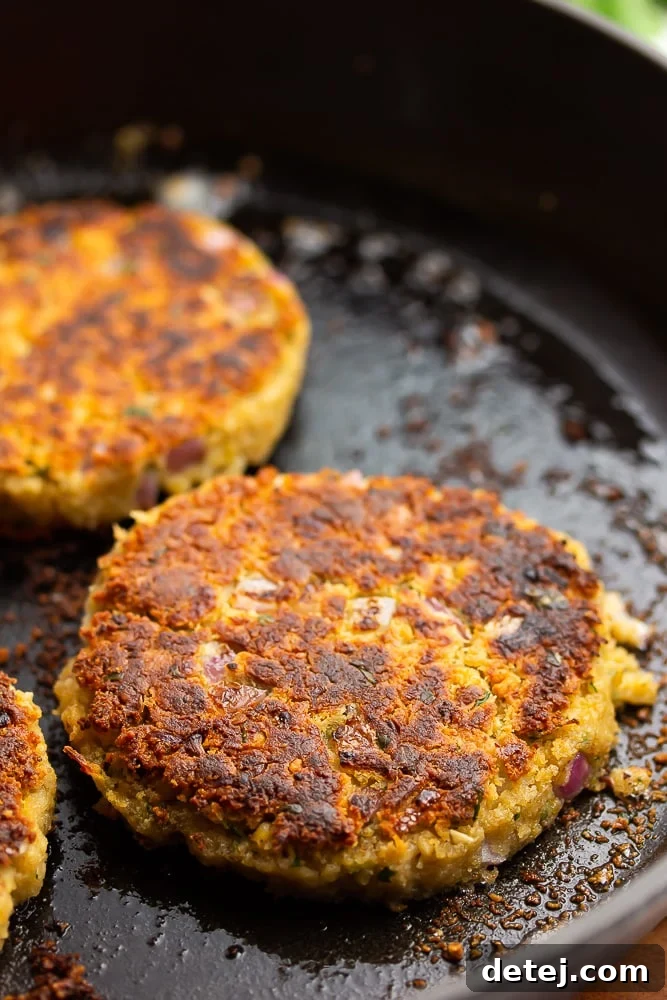 Close-up shot of several vegetarian, bean-based chickpea burgers sizzling to golden perfection in a black cast iron pan on a stovetop.
