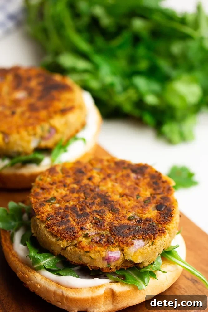 An appetizing close-up of open-faced chickpea burgers on buns, generously topped with fresh green arugula and other vibrant vegetables, highlighting the plant-based patty.