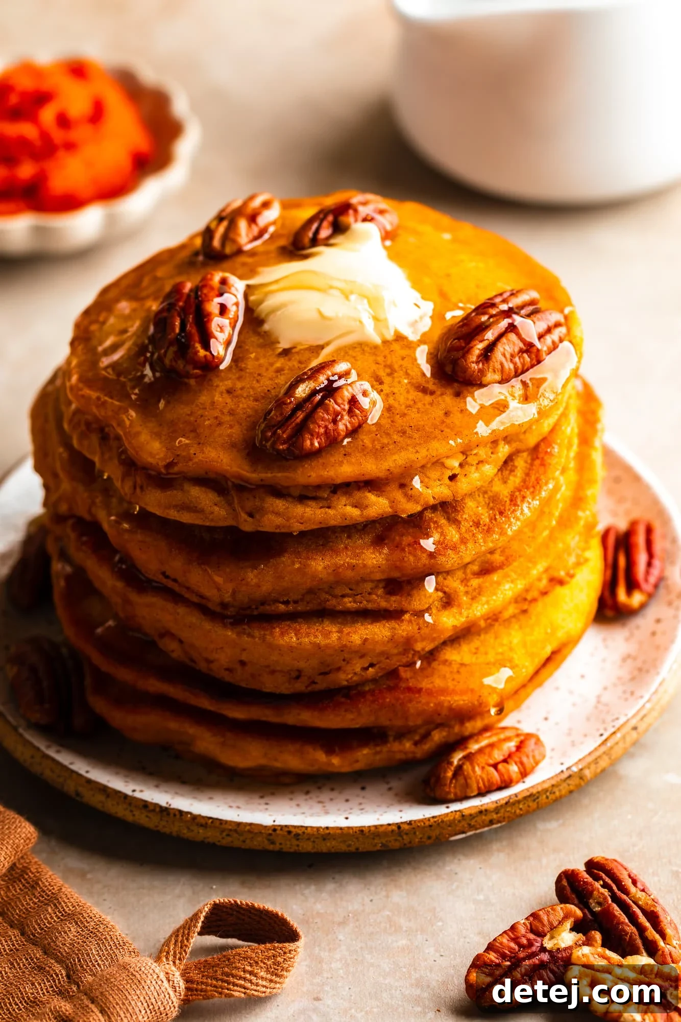 Close-up on a stack of vegan pumpkin pancakes, beautifully adorned with maple syrup, crunchy pecans, and a small square of vegan butter.
