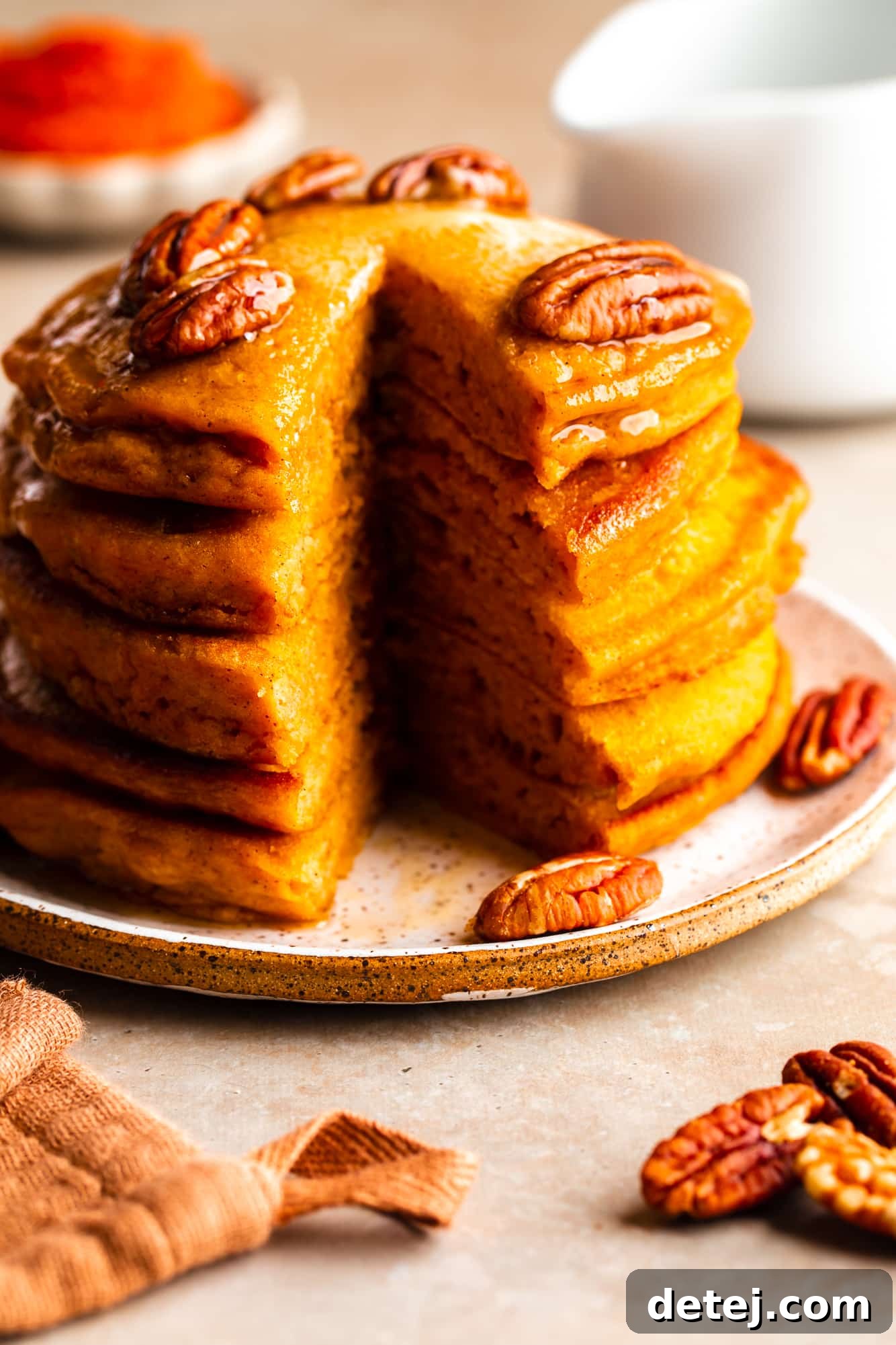 Close-up on a half-eaten stack of vegan pumpkin pancakes, revealing their fluffy texture, topped with rich maple syrup and scattered pecans.