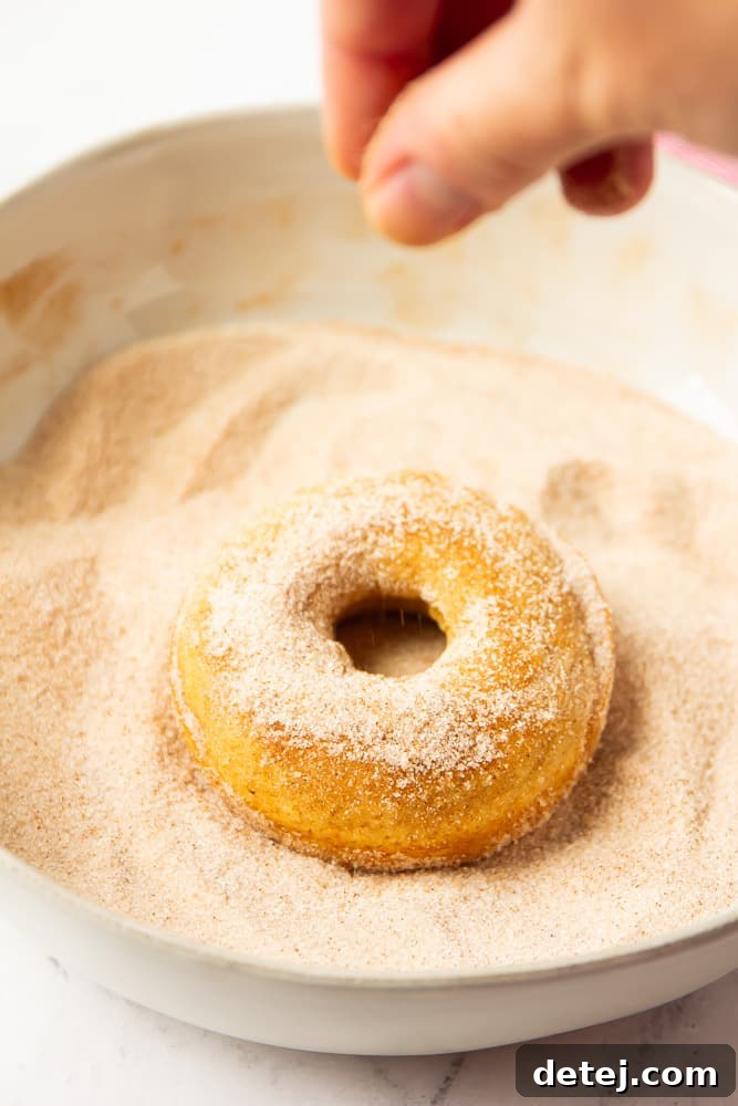a donut being dipped and sprinkled in cinnamon sugar