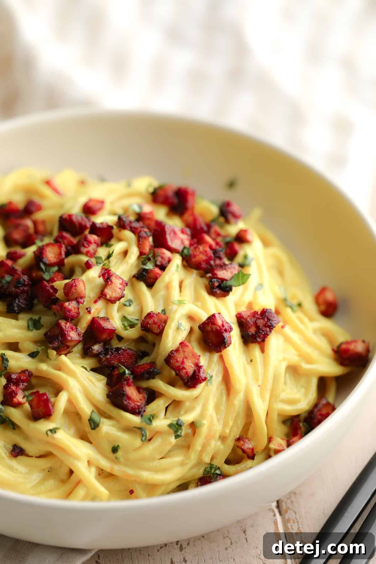 bowl full of yellow noodles with red pieces of tofu on top