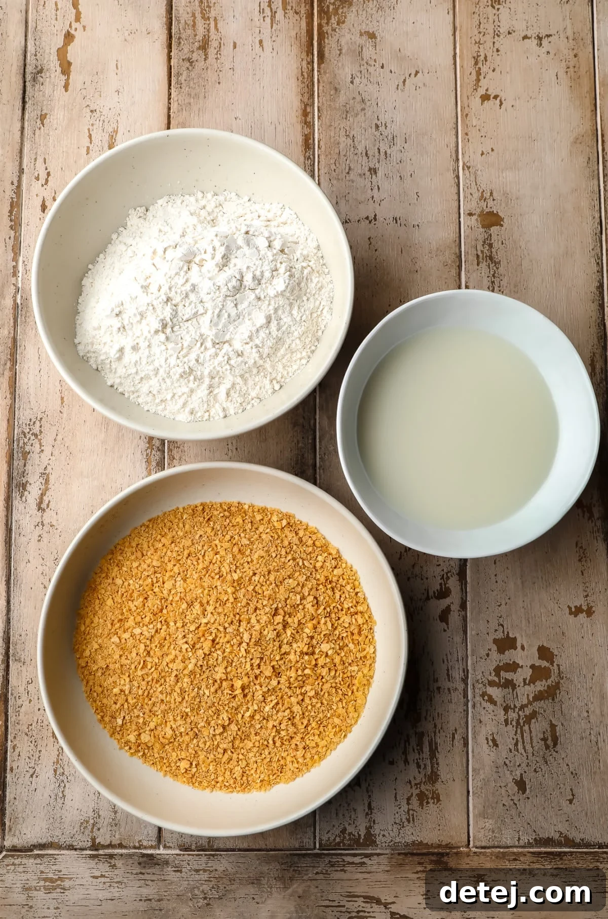 Crispy Plant Based Bites 5 Three bowls on a wooden background: one with breadcrumbs, one with flour, and one with plant milk, set up for a breading station.