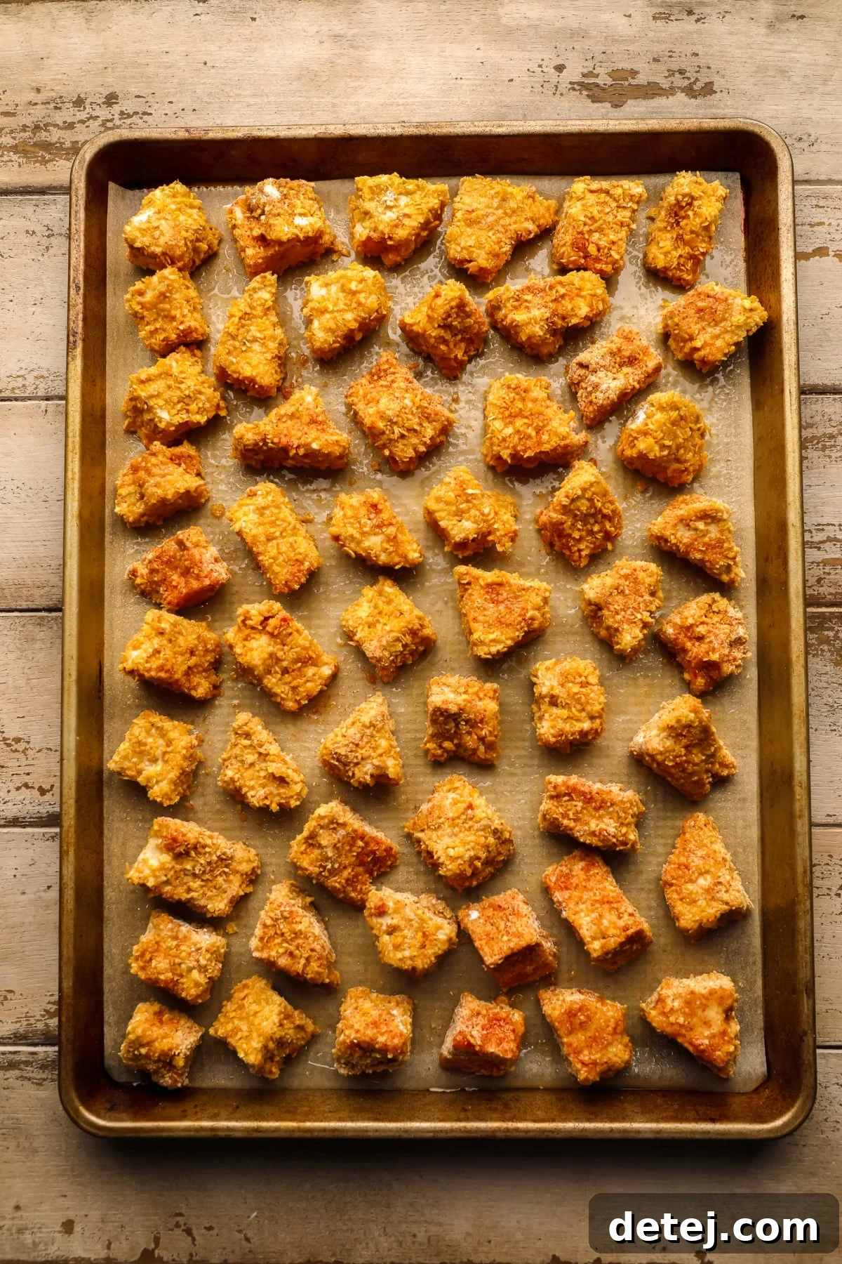 Crispy Plant Based Bites 6 Numerous crispy tofu chunks arranged on a golden baking pan, placed on a wooden surface.