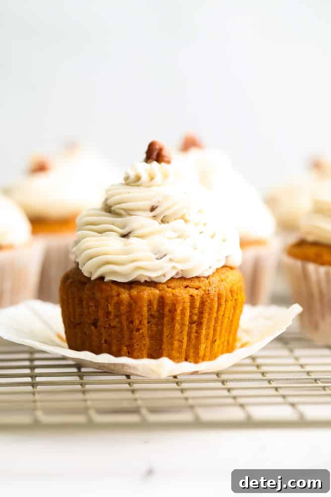 an orange cupcake with frosting, more in background, pecan on top