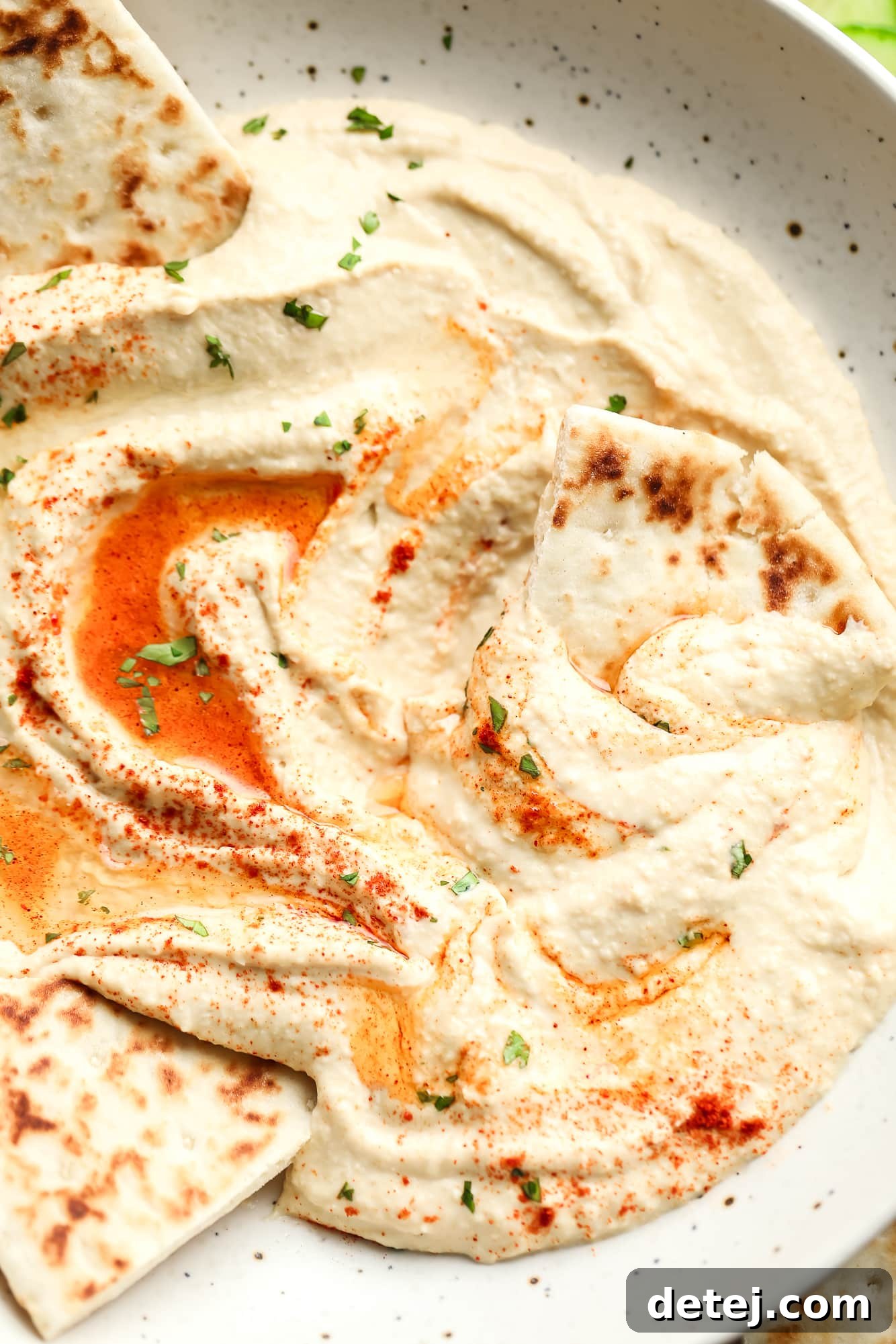 hummus topped with paprika and oil in a white bowl with pita bread on the side.