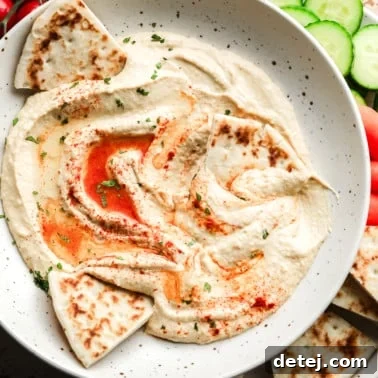 hummus topped with paprika and oil in a white bowl with pita bread on the side.