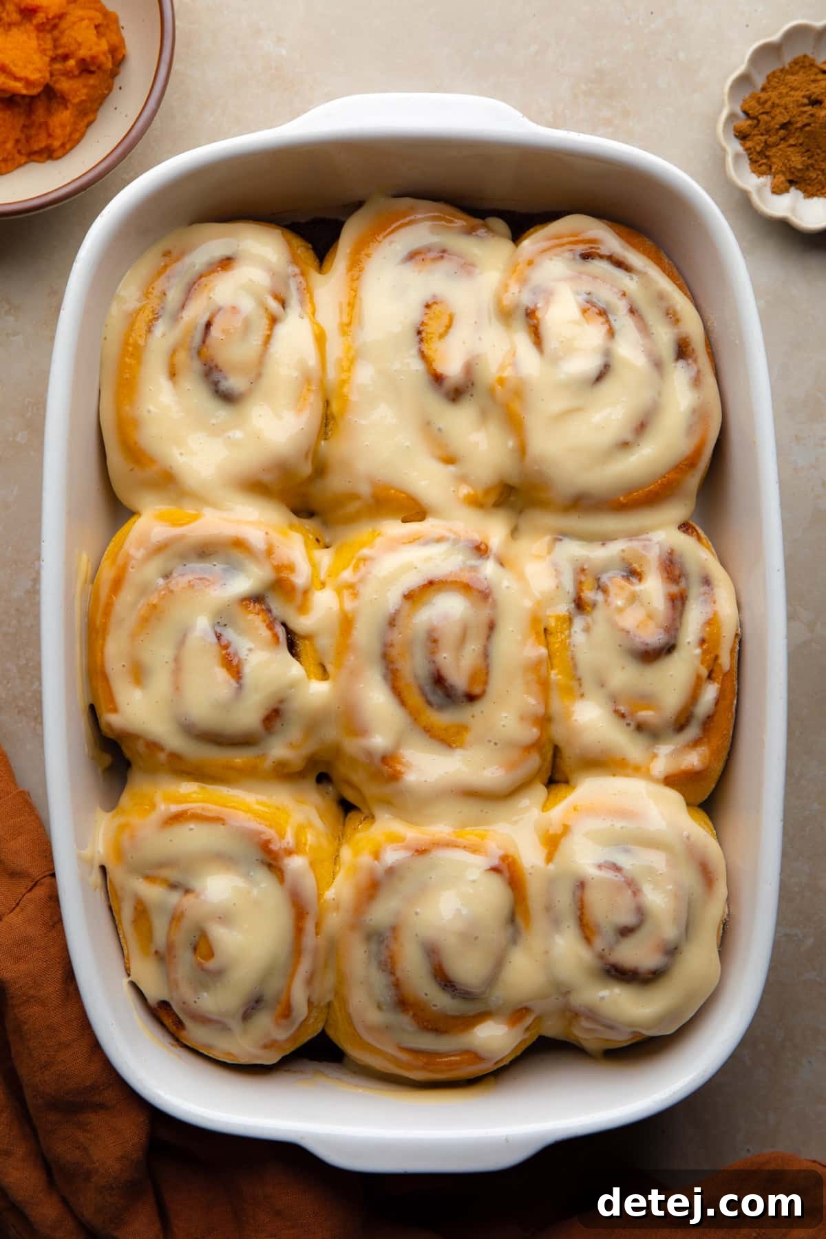 9 orange cinnamon rolls in dish with beige background