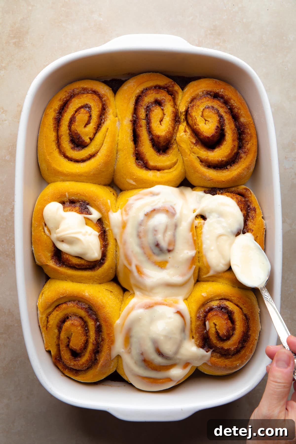 orange rolls with cream cheese frosting being spread on them