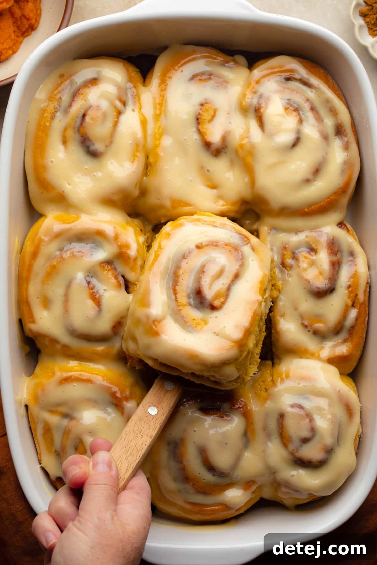 vegan pumpkin cinnamon rolls in white dish with spatula taking one out