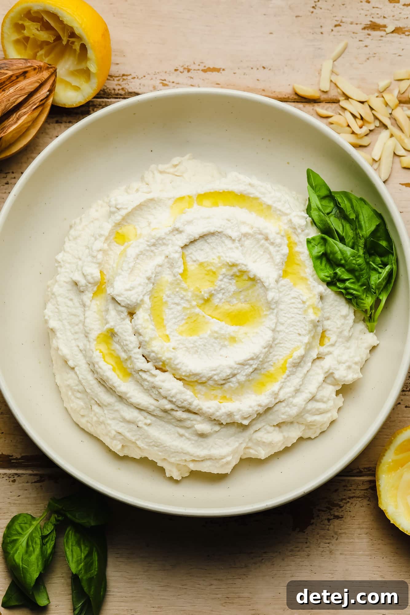 Vegan Ricotta cheese in a white bowl with olive oil drizzled on top and basil leaves on the side.