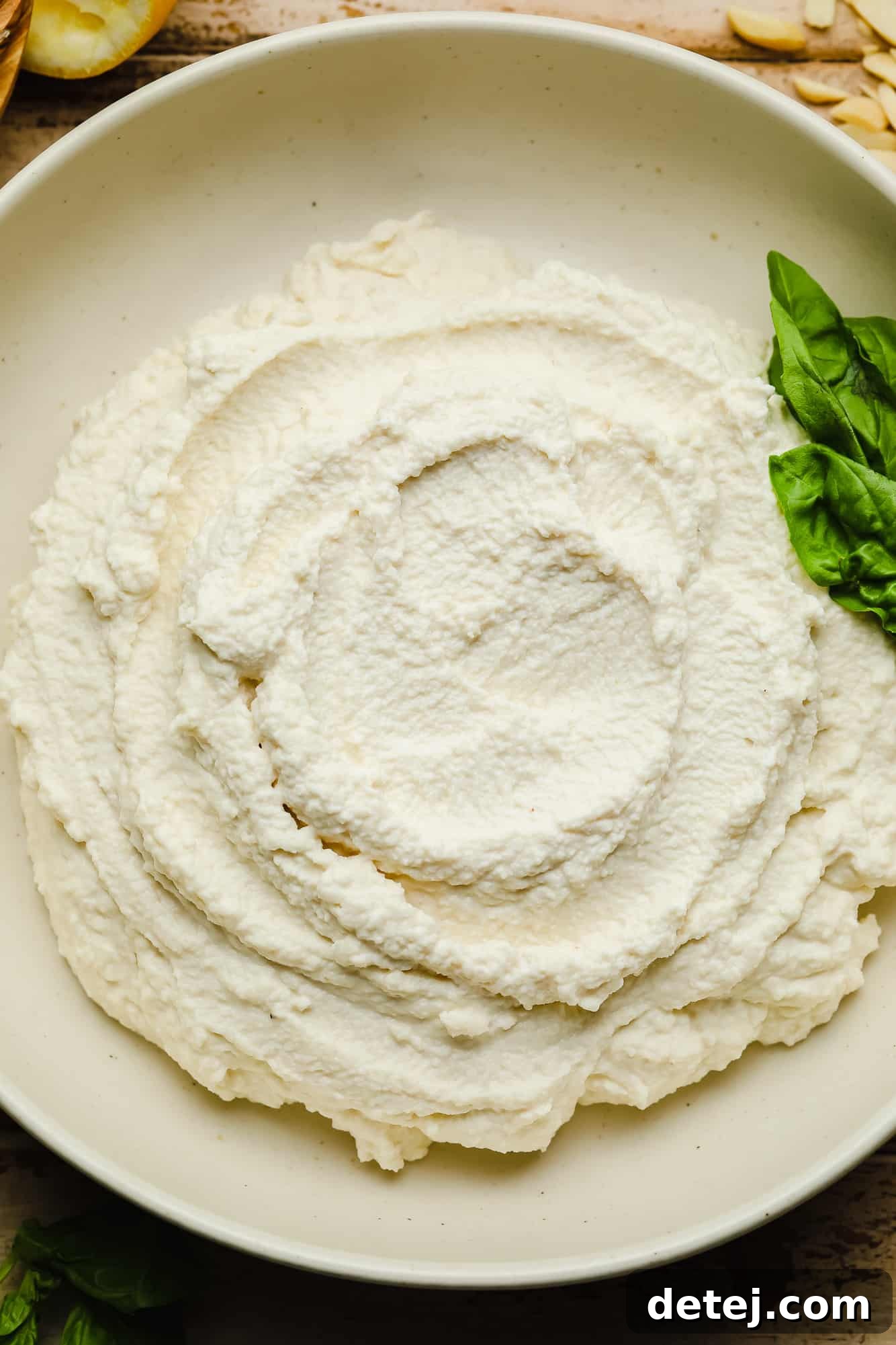Vegan Ricotta cheese in a white bowl with basil leaves on the side.