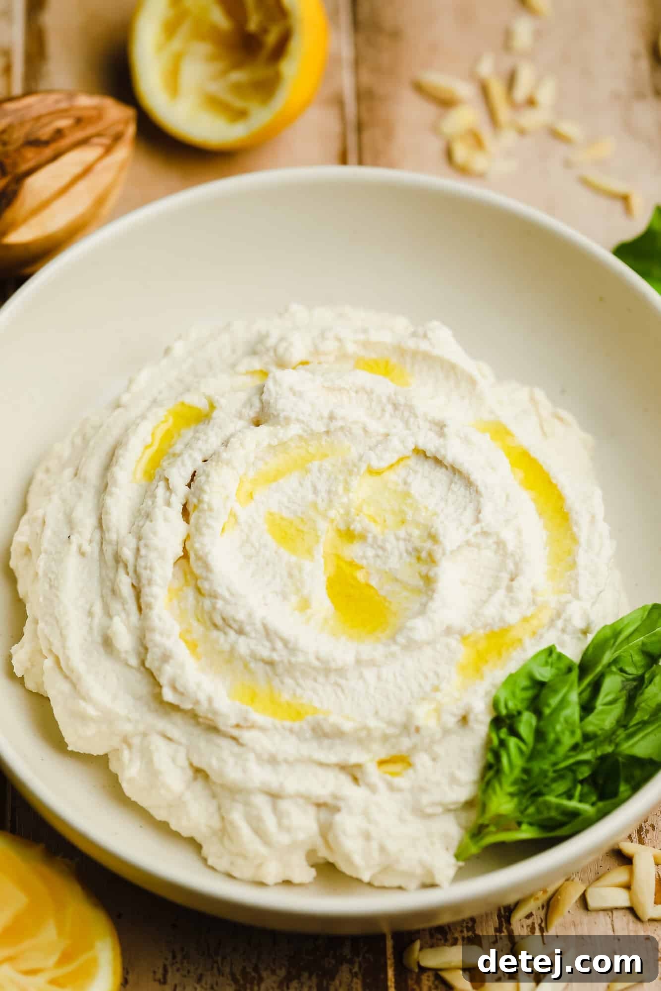Vegan Ricotta cheese in a white bowl with olive oil drizzled on top and basil leaves on the side.