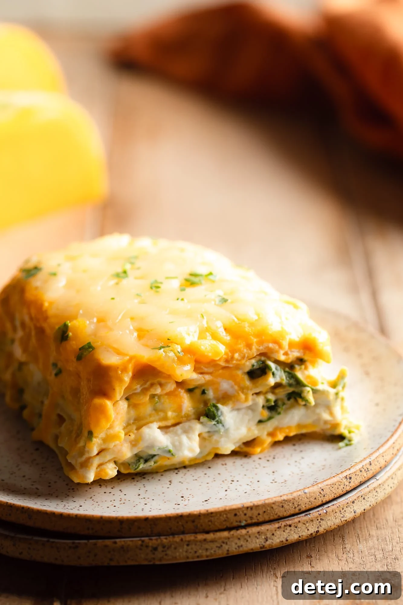 Close up on a slice of creamy vegan butternut squash lasagna, showing distinct layers of pasta, sauce, ricotta, and kale, on a white plate with a fork.