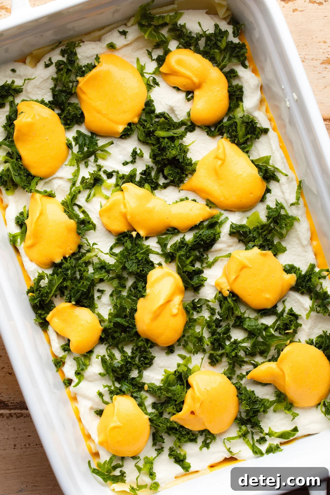 Assembling a vegan butternut squash lasagna in a casserole dish, showing layers of noodles, ricotta, and sauce.