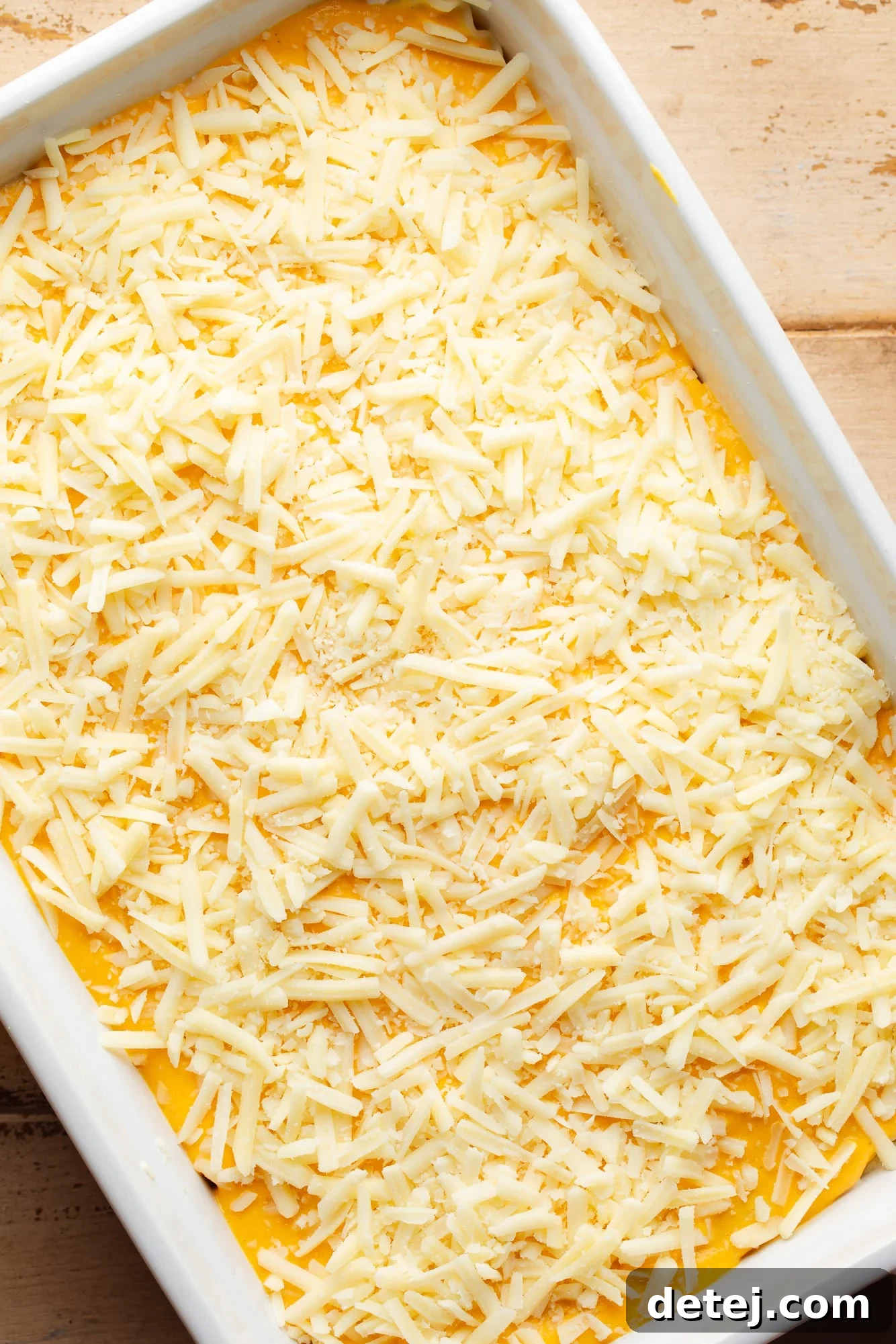 Sprinkling vegan mozzarella cheese over the top layer of an assembled butternut squash lasagna before baking.