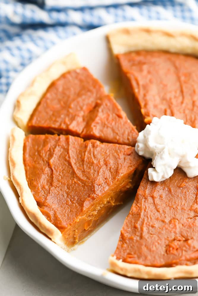 A beautiful vegan sweet potato pie in a white pie dish, with a golden-brown crust and smooth orange filling, a small slice cut out