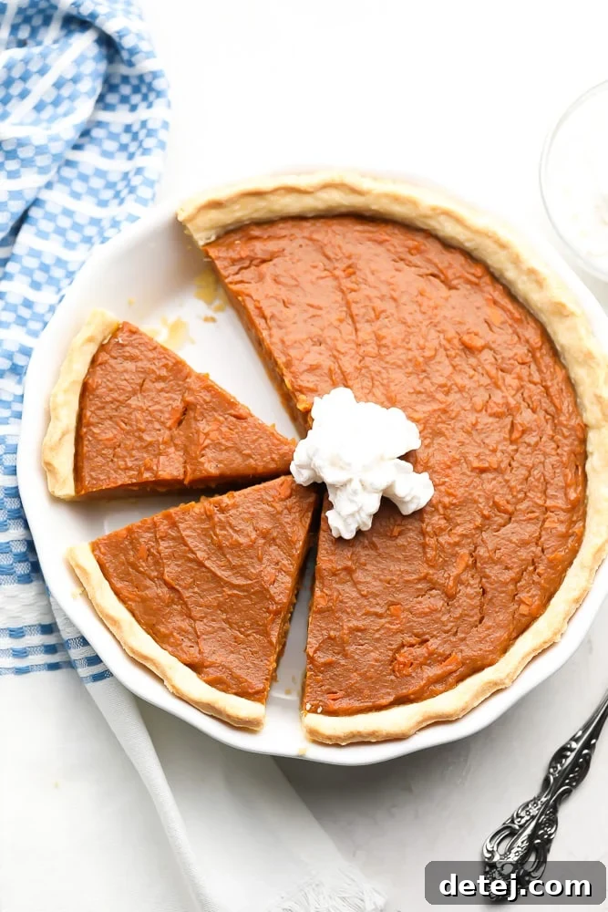 An overhead view of a delicious vegan sweet potato pie with several slices already cut, presented on a white background with a blue linen towel