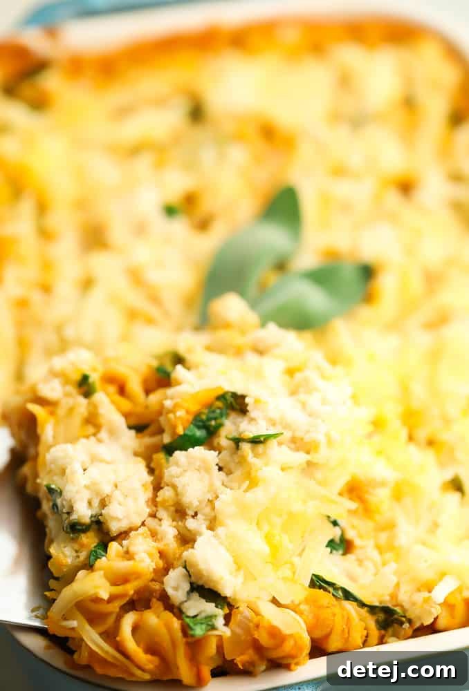 A generous serving of creamy pumpkin pasta bake being lifted from a casserole dish, showcasing rich sauce, vegan ricotta, and melted cheese.