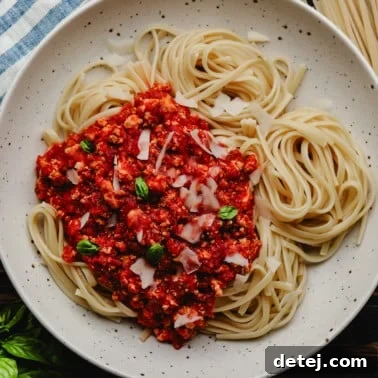 A square image of a bowl filled with an abundance of noodles and rich red vegan bolognese sauce on one side of the pasta.
