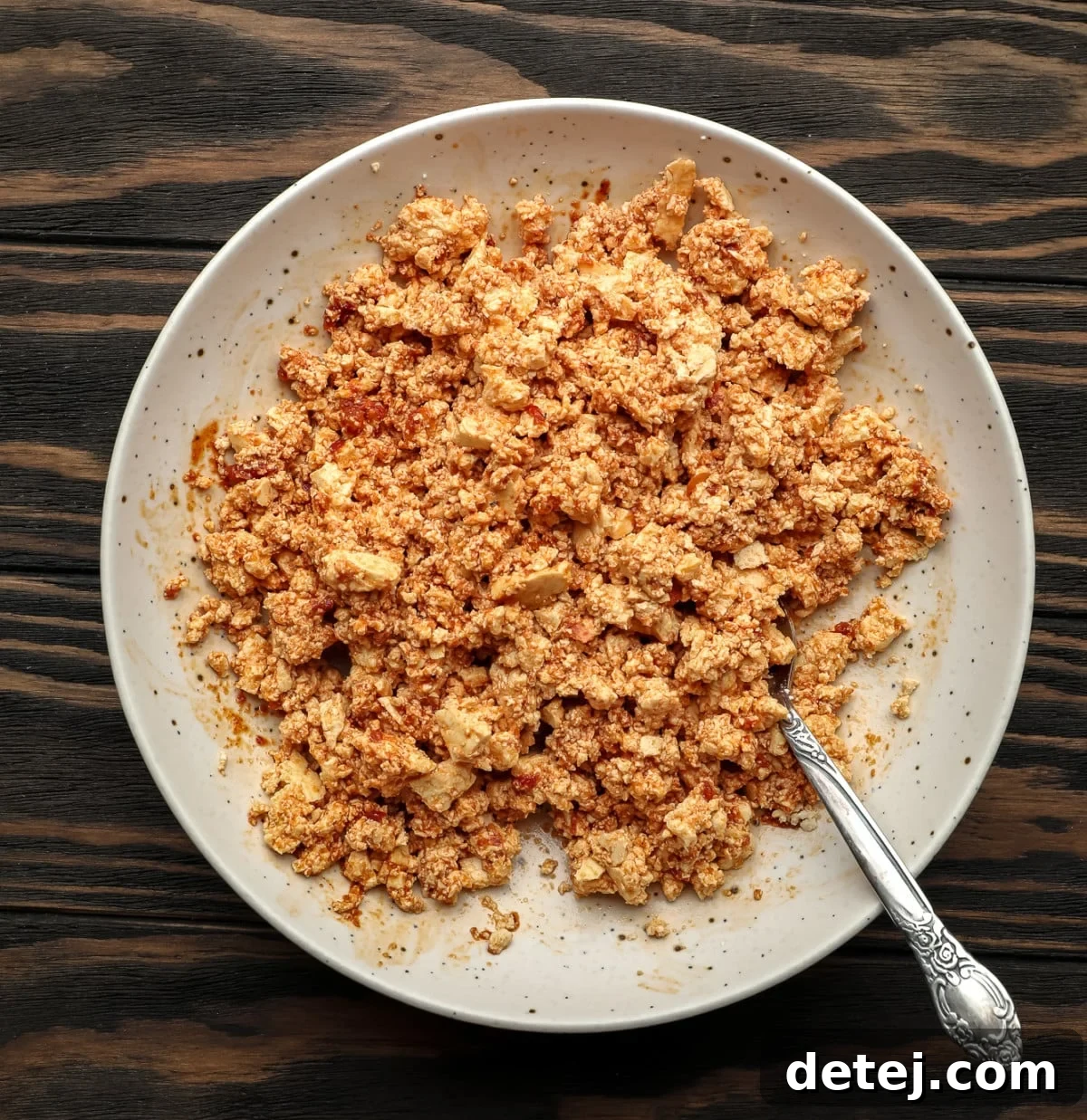 Tofu crumbles mixed with a reddish sauce in a speckled bowl, ready for baking.