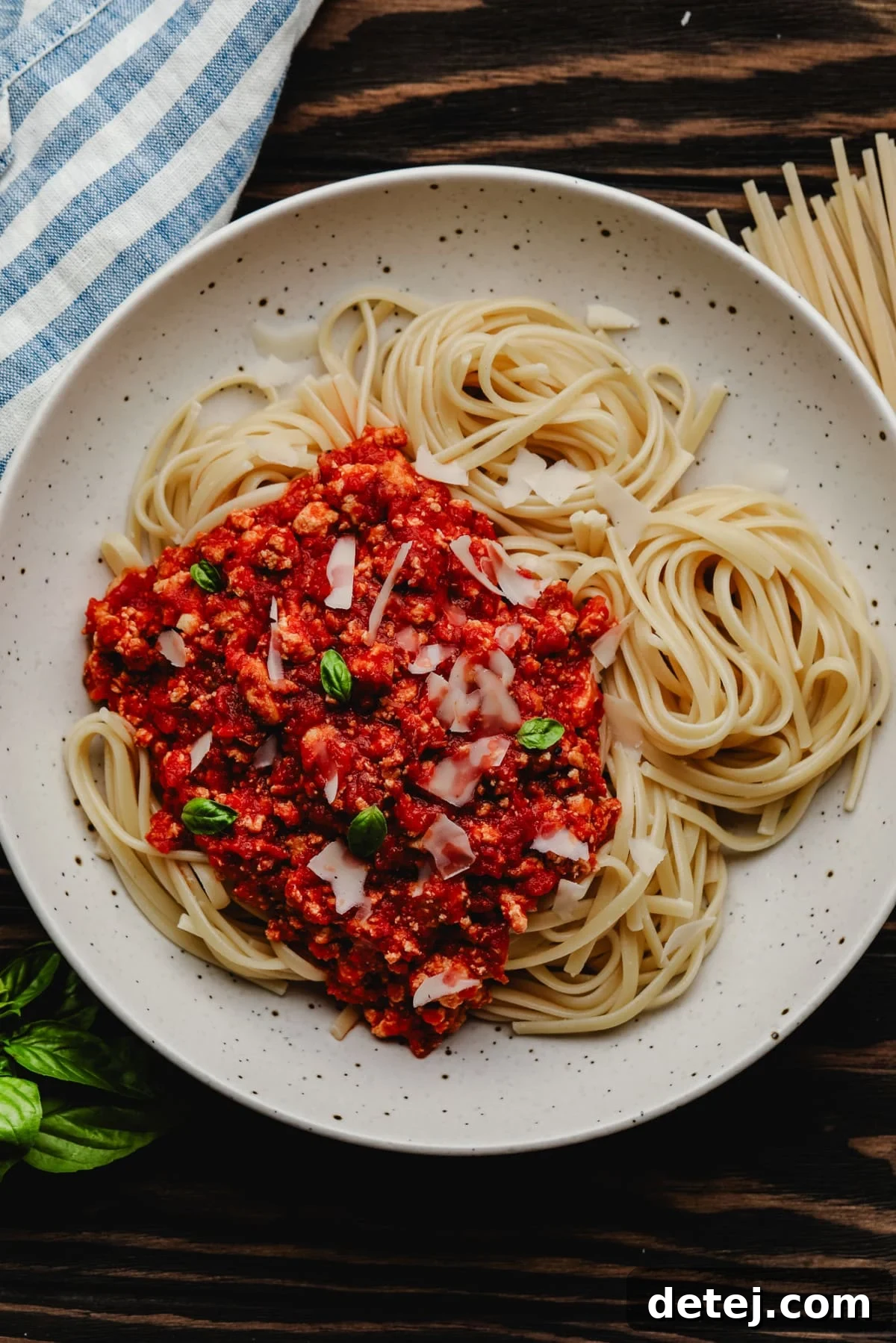 A speckled bowl filled with perfectly cooked pasta and rich vegan bolognese sauce, placed on a rustic wooden background.