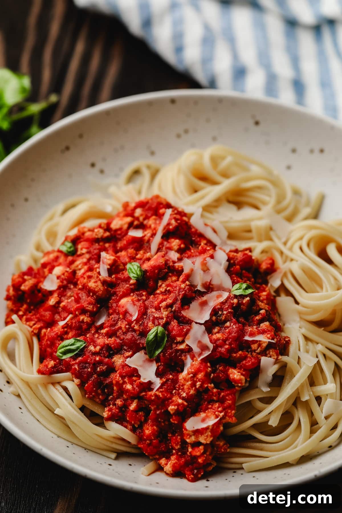 A beautifully presented dish of noodles with vegan bolognese sauce, garnished with vegan parmesan and fresh basil leaves, on a rustic wooden background.