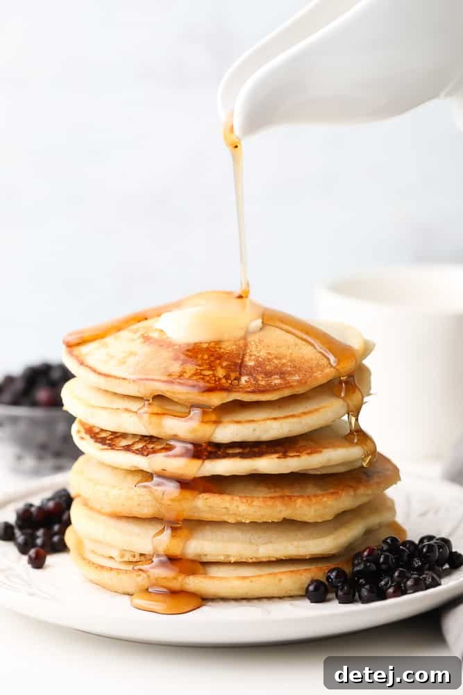 Golden stack of fluffy vegan buckwheat pancakes with syrup being poured generously over them, ready for a delicious breakfast.