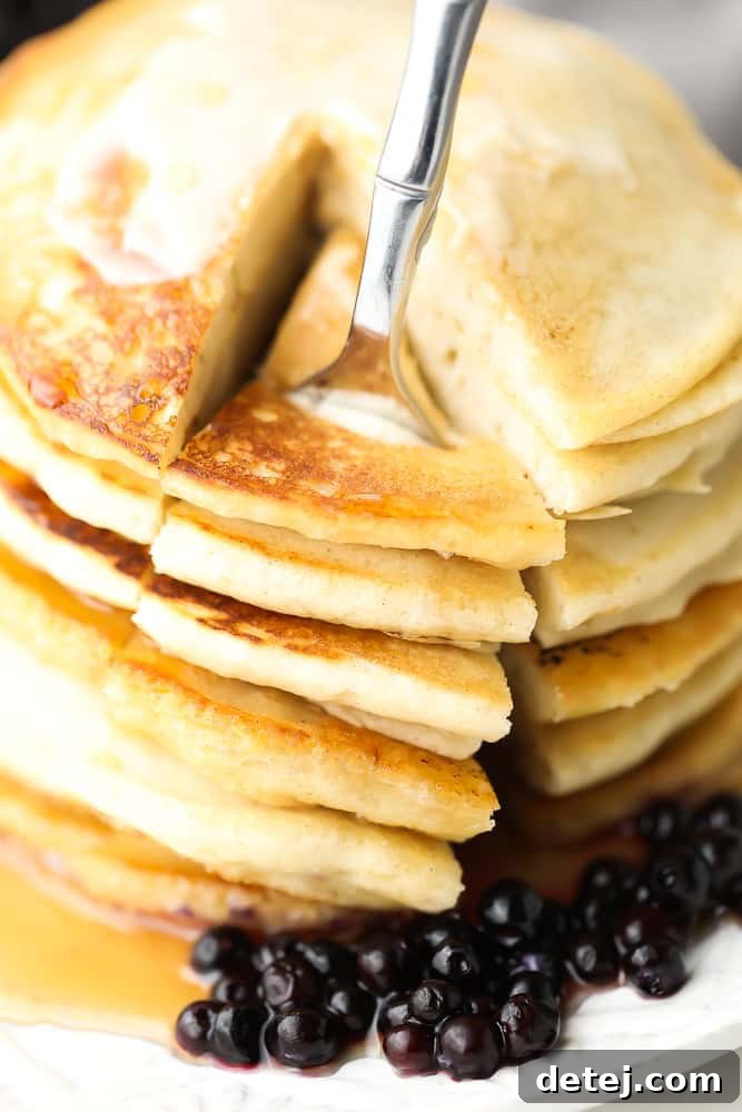 A fork taking a large bite out of a stack of fluffy vegan buckwheat pancakes, revealing their tender interior.