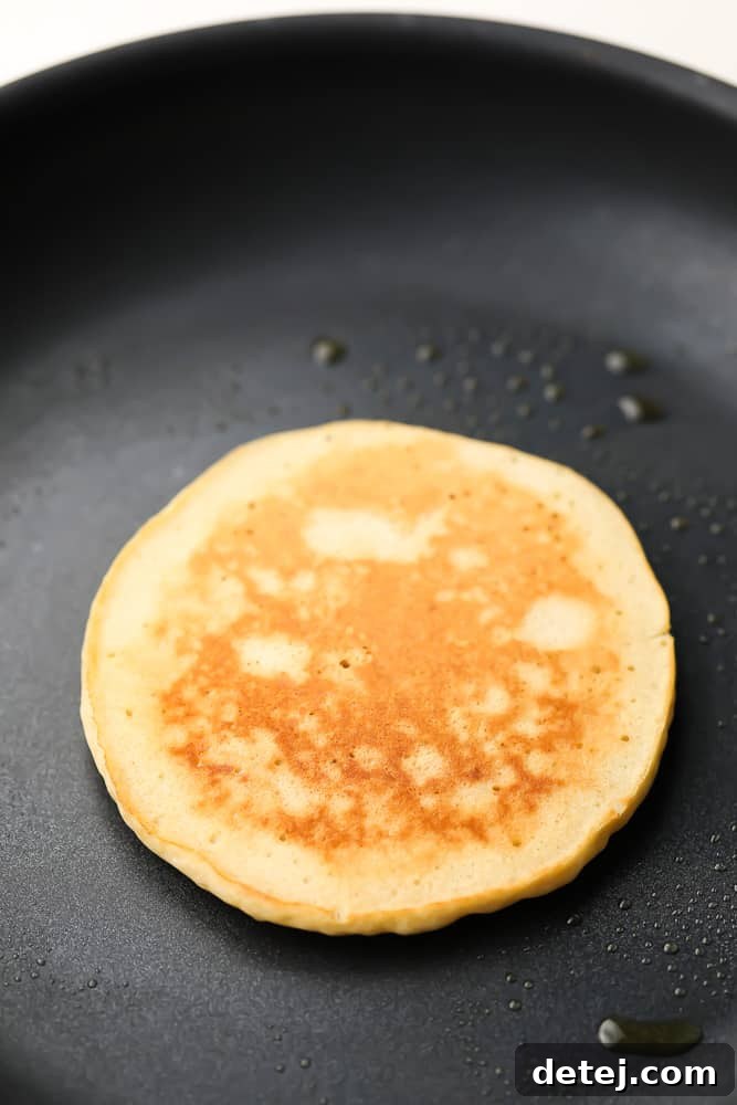 Several vegan buckwheat pancakes cooking on a griddle, showing the golden-brown underside after flipping.