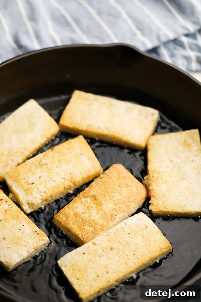Slabs of tofu being pan-fried until golden brown in a skillet.