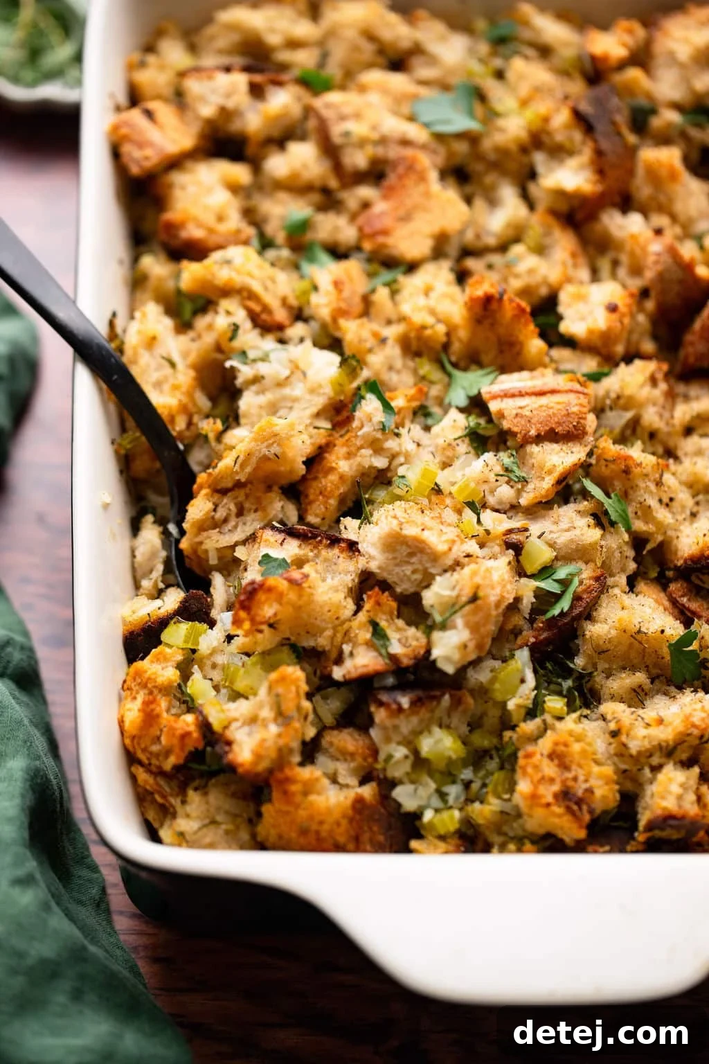 Ultimate Vegan Stuffing 2 Close-up of golden brown vegan stuffing in a white casserole dish with a black serving spoon.