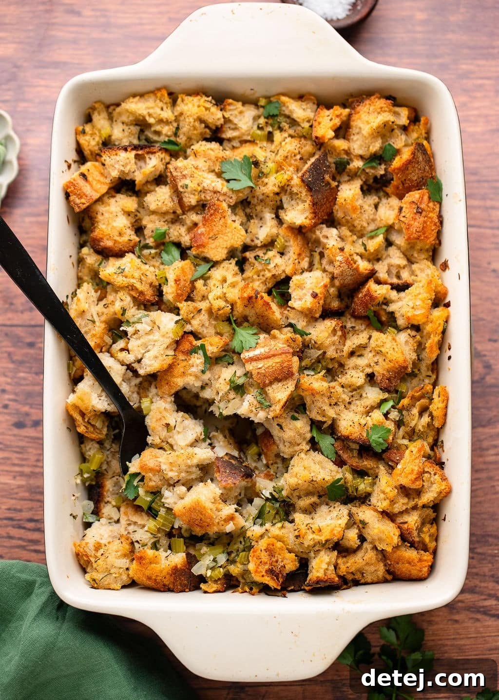 Ultimate Vegan Stuffing 3 Baked vegan stuffing in a white ceramic casserole dish with a black serving spoon, ready to be served.