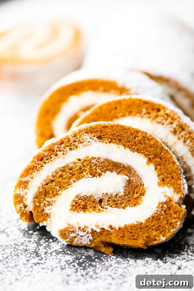 Close-up of perfectly sliced vegan pumpkin roll pieces, showing the distinct spiral of cake and creamy frosting, dusted with powdered sugar.