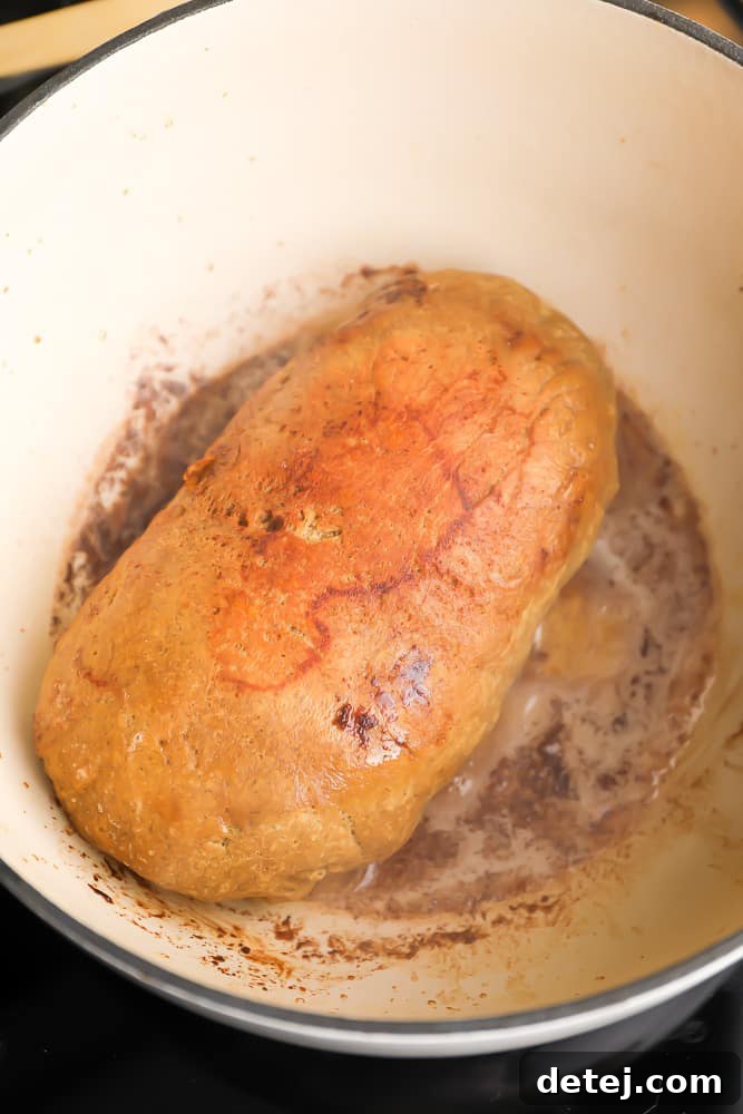 A vegan turkey loaf being browned to a golden crisp in a white skillet with melted vegan butter and soy sauce.
