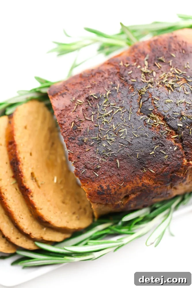 An overhead view of a vegetarian turkey loaf, partially sliced, surrounded by fresh sage leaves on a rustic serving board.